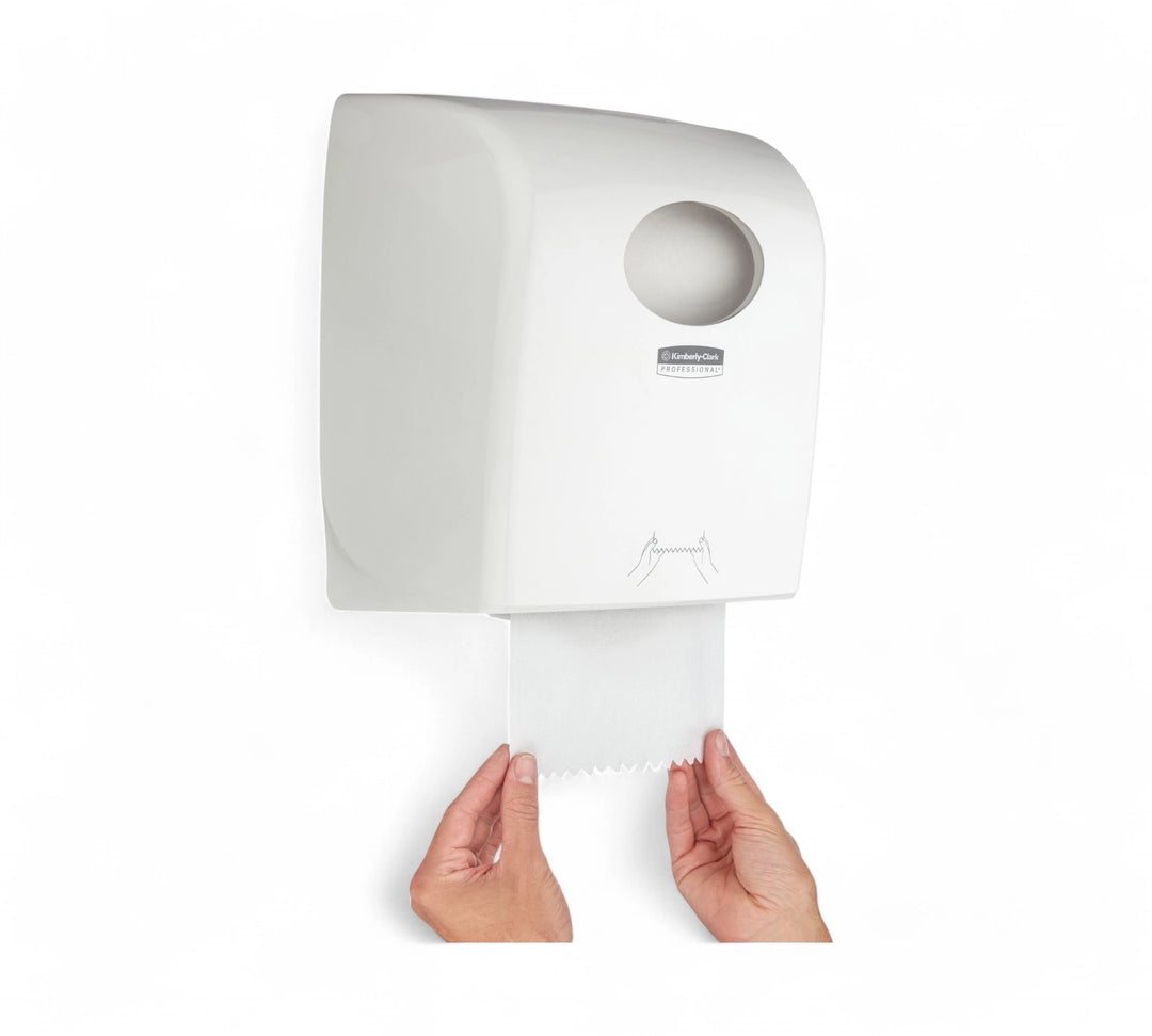 Wall-mounted Kimberly-Clark Aquarius paper towel dispenser with towel being dispensed by two hands, showing serrated edge and clean pull motion.
