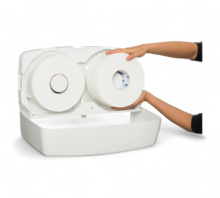 Open view of the KIMBERLY-CLARK PROFESSIONAL AQUARIUS Twin Jumbo Roll Dispenser (70210), showing a person loading a jumbo toilet paper roll into the right-hand side compartment while another roll is already installed on the left.
