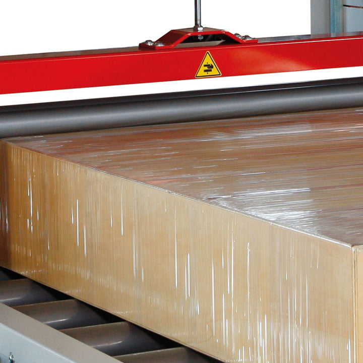 Cardboard box securely wrapped in stretch film moving through AT-A horizontal wrapping machine on roller conveyor