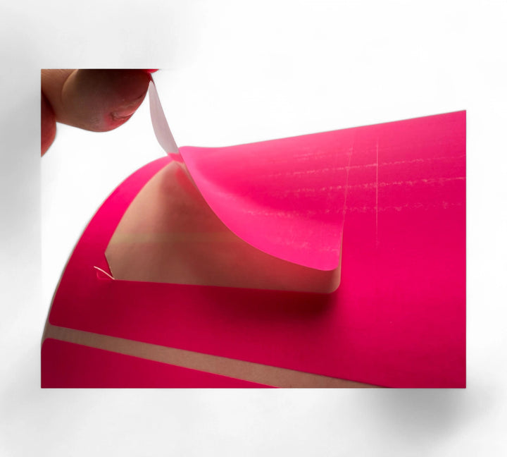 Close-up of a pink direct thermal label being peeled back from the roll, highlighting the adhesive underside and vibrant label color