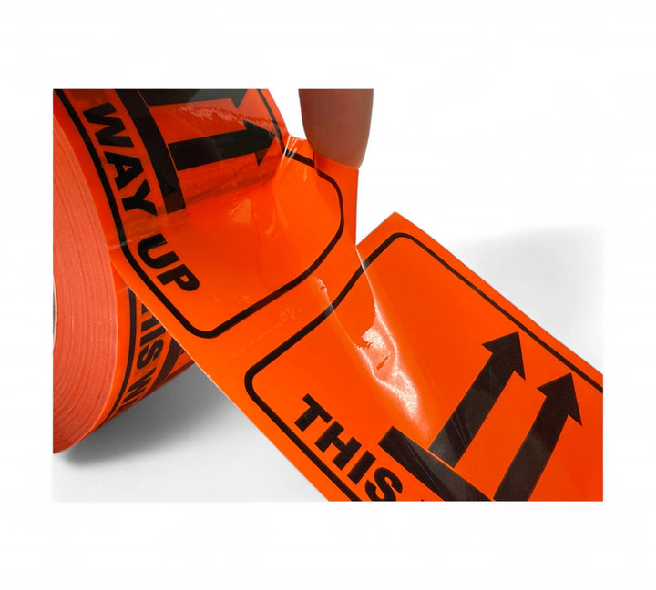 Close-up of perforated This Way Up warning labels in bold black print on fluro orange background with upward arrow icons