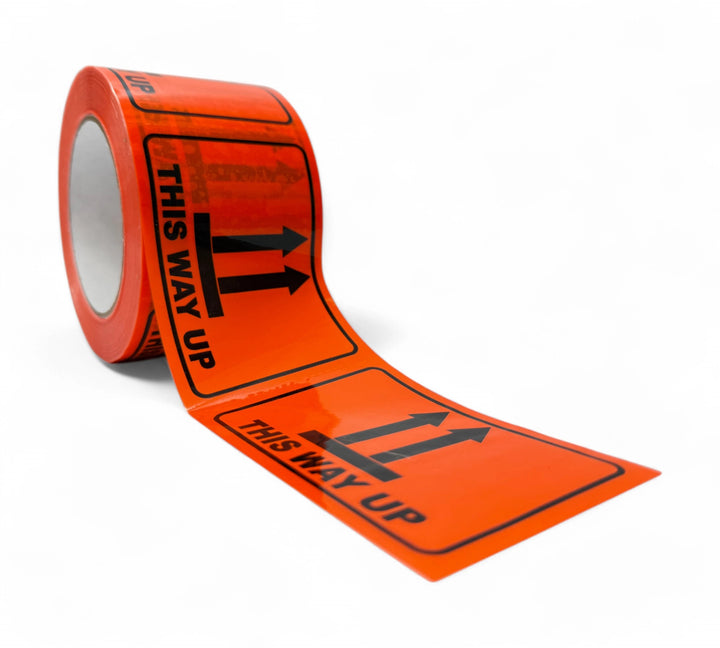 Roll of fluro orange This Way Up labels with bold black print and upward arrows, unspooled to show multiple warning stickers in sequence